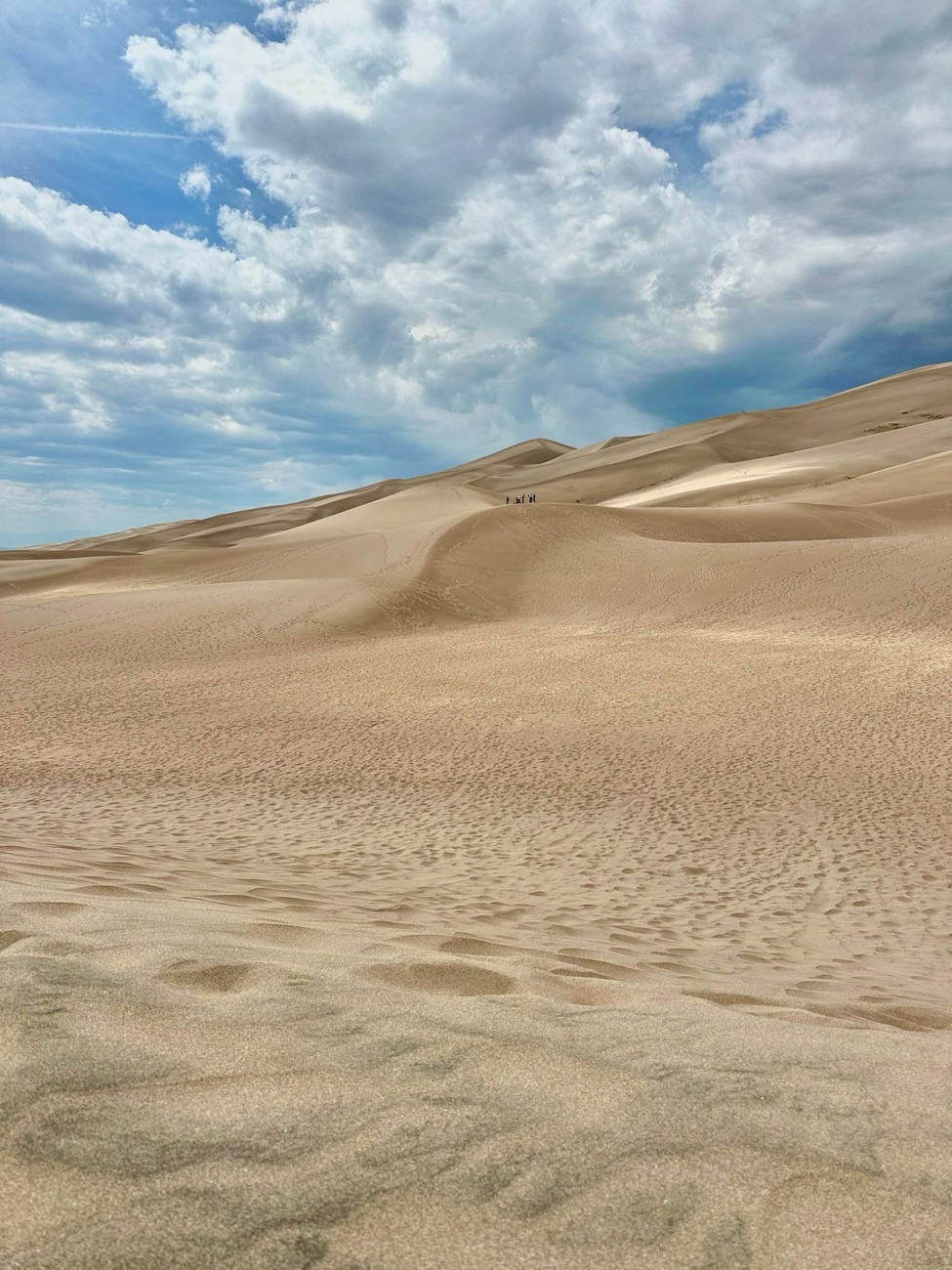 Dunes de sable sous un ciel nuageux, quelques silhouettes au loin